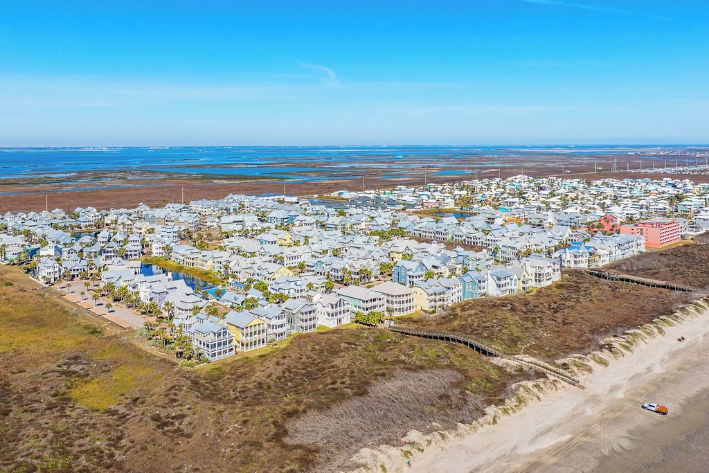 Vue aérienne d’un quartier résidentiel situé sur la côte, avec des maisons, une plage et un ciel d égagé.