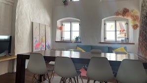 Et spiseområde med et langt bord, flere stole og to vinduer med gardiner.