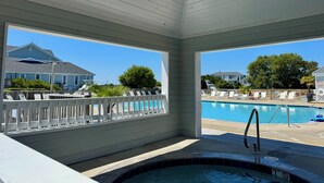 A covered pool area with a hot tub, lounge chairs, and a view of a residential neighborhood. - A Pirates Life - Fishing, Boat Slip, Pool, Gym!  (Manteo)