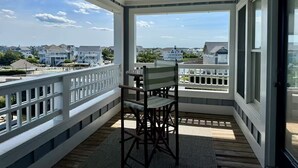 A covered balcony with a table and chair, white railings, and a view of houses and water. - A Pirates Life - Fishing, Boat Slip, Pool, Gym!  (Manteo)