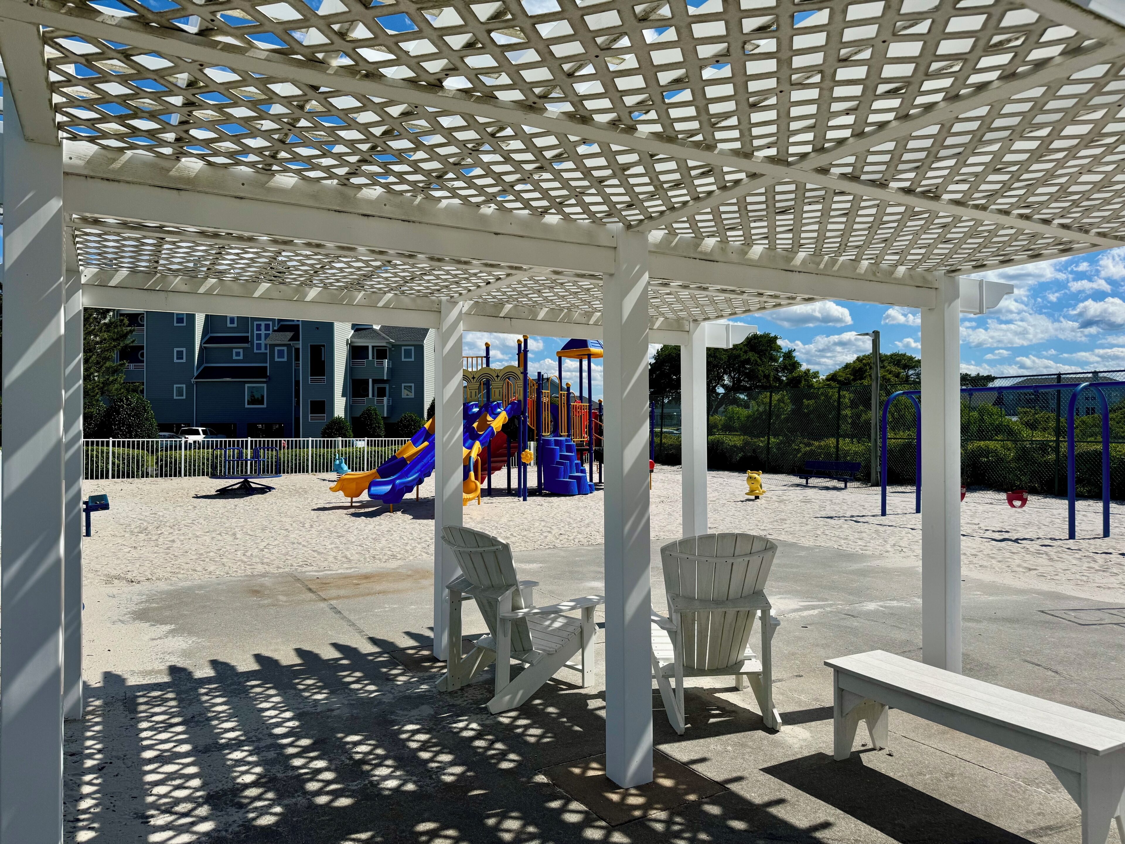 Ein überdachter Außenbereich mit einem Spielplatz, Bänken und einem Gebäude im Hintergrund.