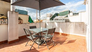 Une terrasse extérieure avec une table et des chaises, un grand parasol et une vue sur le paysage urbain.