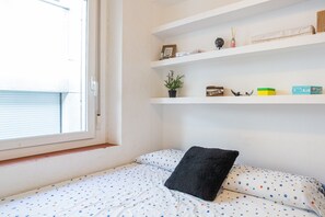 Et soveværelse med en seng, et vindue og en reol med diverse genstande.