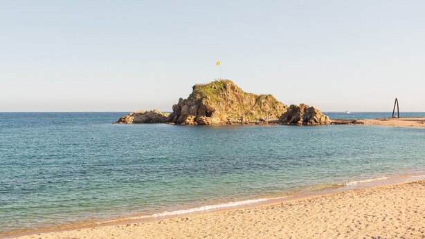 Une plage avec une île rocheuse, une eau cristalline et un rivage sablonneux.