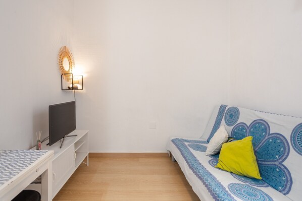 A room with a bed, a TV on a stand, a wall-mounted light, and a desk with a chair.