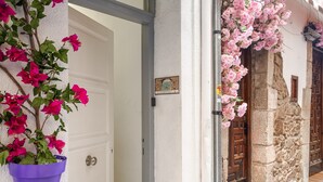 Une porte blanche ornée d’un pot de fleurs suspendu bleu et de fleurs roses.