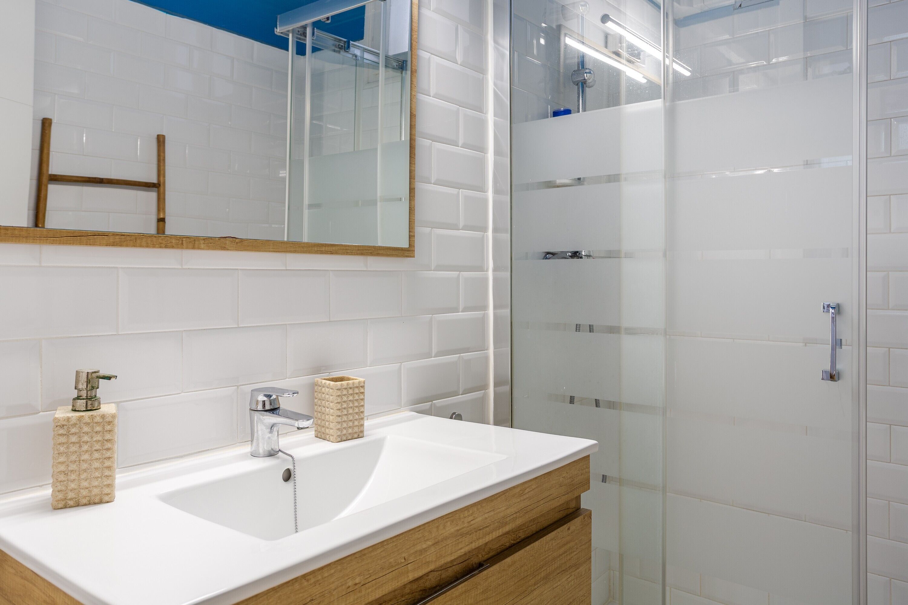 Een badkamer met een wit wastafelmeubel, een spiegel en een douchecabine van glas.