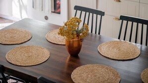 A kitchen with white cabinets, a stove, and hanging pots. There is a table with woven placemats and a vase with flowers. - 18th Century Cottage w/ heated pool 2 hrs from NYC (Rosendale)