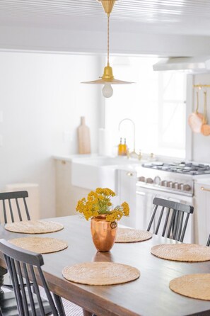 A dining area with a copper vase of yellow flowers on a wooden table, surrounded by black chairs and woven placemats. - 18th Century Rosendale Cottage w/pool (Rosendale)
