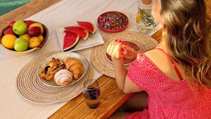 A dining table with a variety of food items, including fruits, a watermelon, and croissants, set on a patio with a view of a pool and greenery. - Charming American Villa – 3BR with AC, WiFi & Pool in Dahab (Dahab)