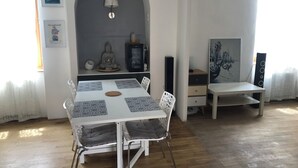 A dining area with a white table, patterned placemats, and metal chairs. A Buddha statue and a lantern are on the wall behind the table.
