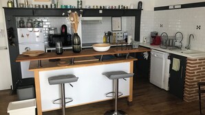 A modern kitchen with a central island, bar stools, a refrigerator, and a brick accent wall.