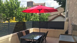 A patio with a glass table and chairs, a red umbrella, and a black fence.