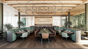 Een ruim restaurant met een lange gedeelde tafel, zitjes en een moderne kroonluchter.
