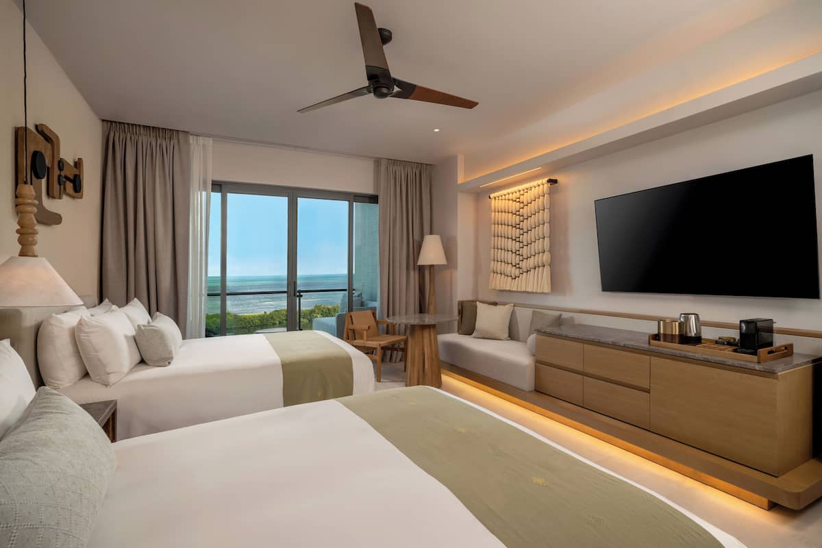 Een moderne hotelkamer met twee bedden, een bank, een televisie en uitzicht op de oceaan.