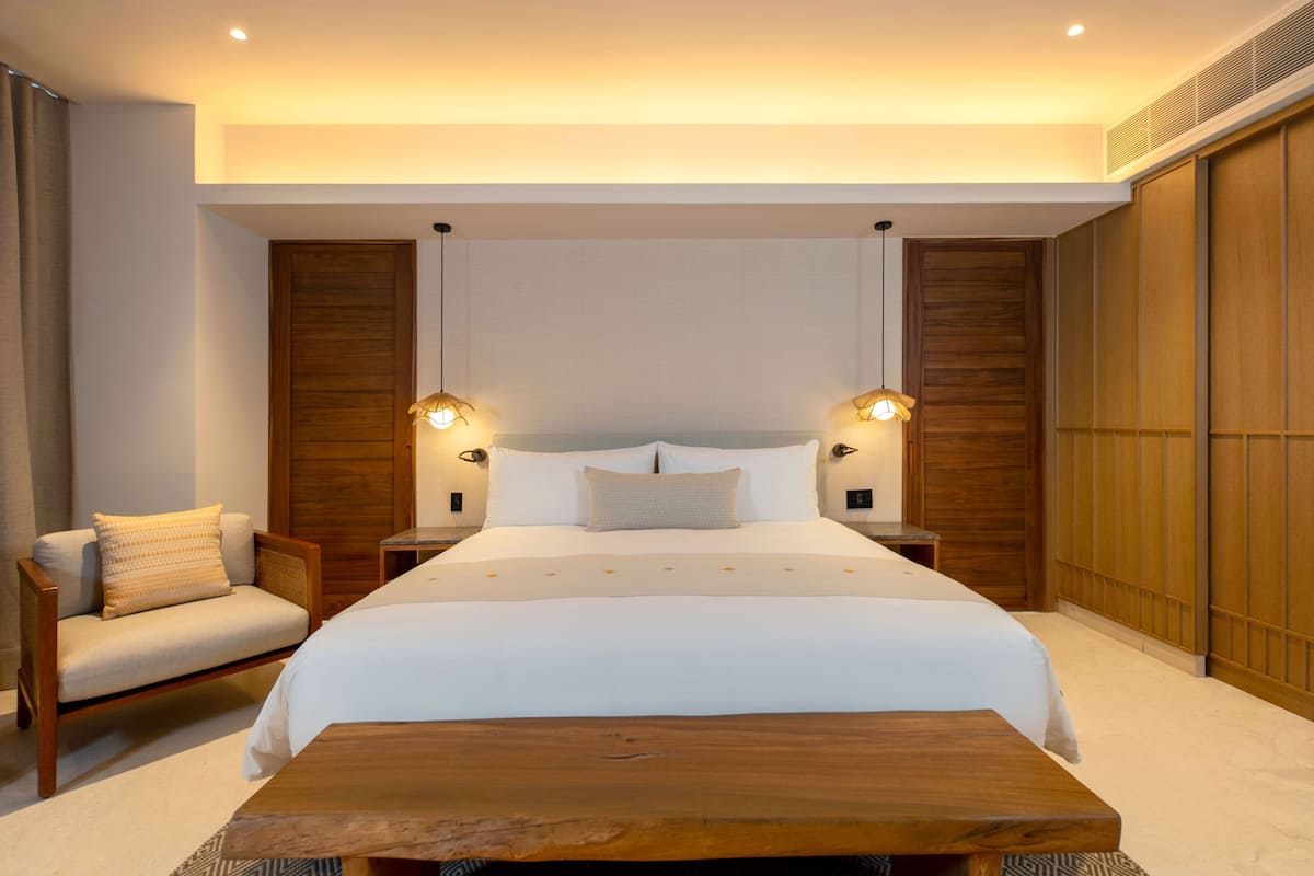 Een hotelkamer met een groot bed, een houten hoofdbord, twee bedlampen, een nachtkastje van hout, een stoel en een houten salontafel.