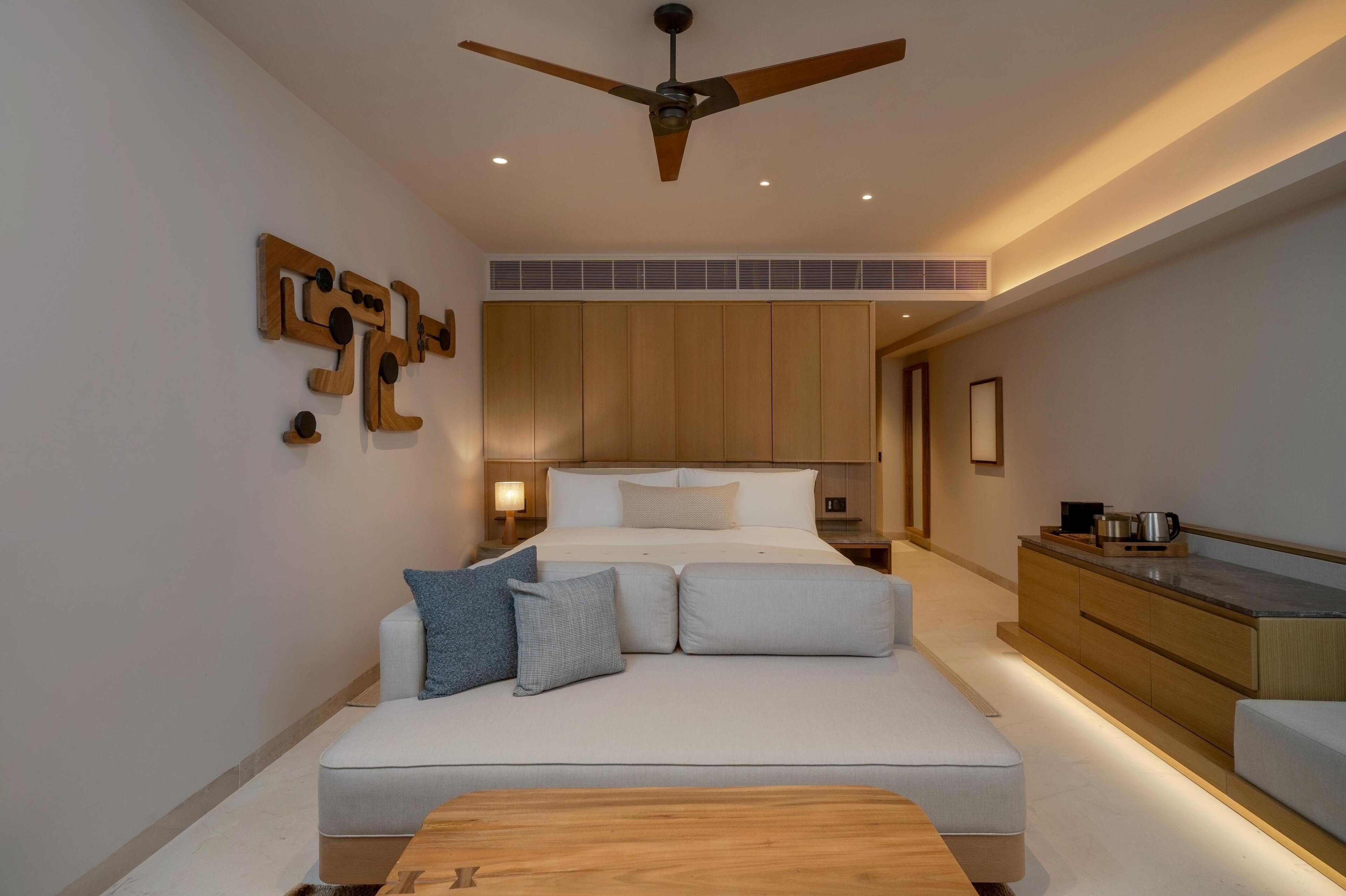 A modern bedroom with a large bed, a ceiling fan, and a kitchenette area.