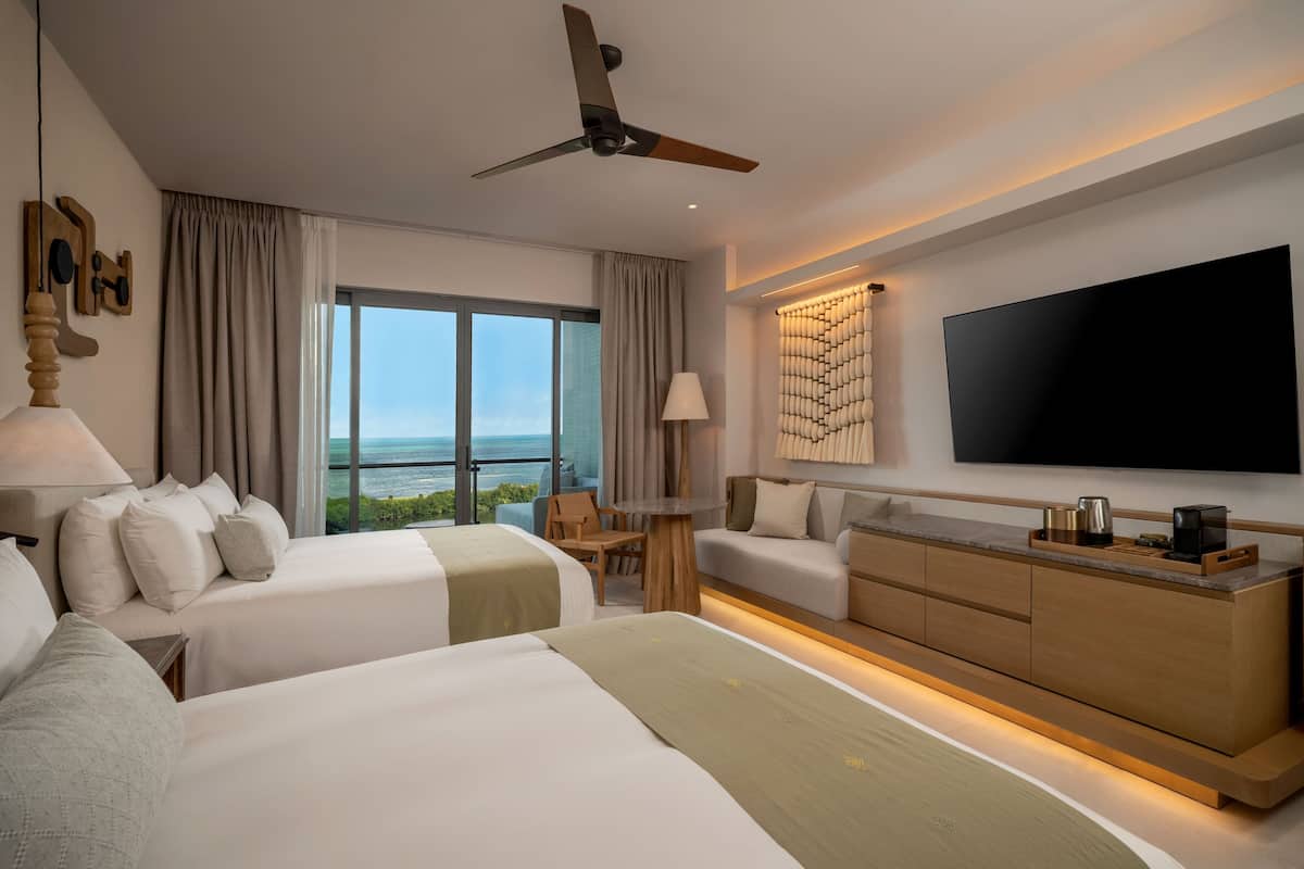 Een moderne hotelkamer met twee bedden, een grote televisie, een plafondventilator en uitzicht op de oceaan.