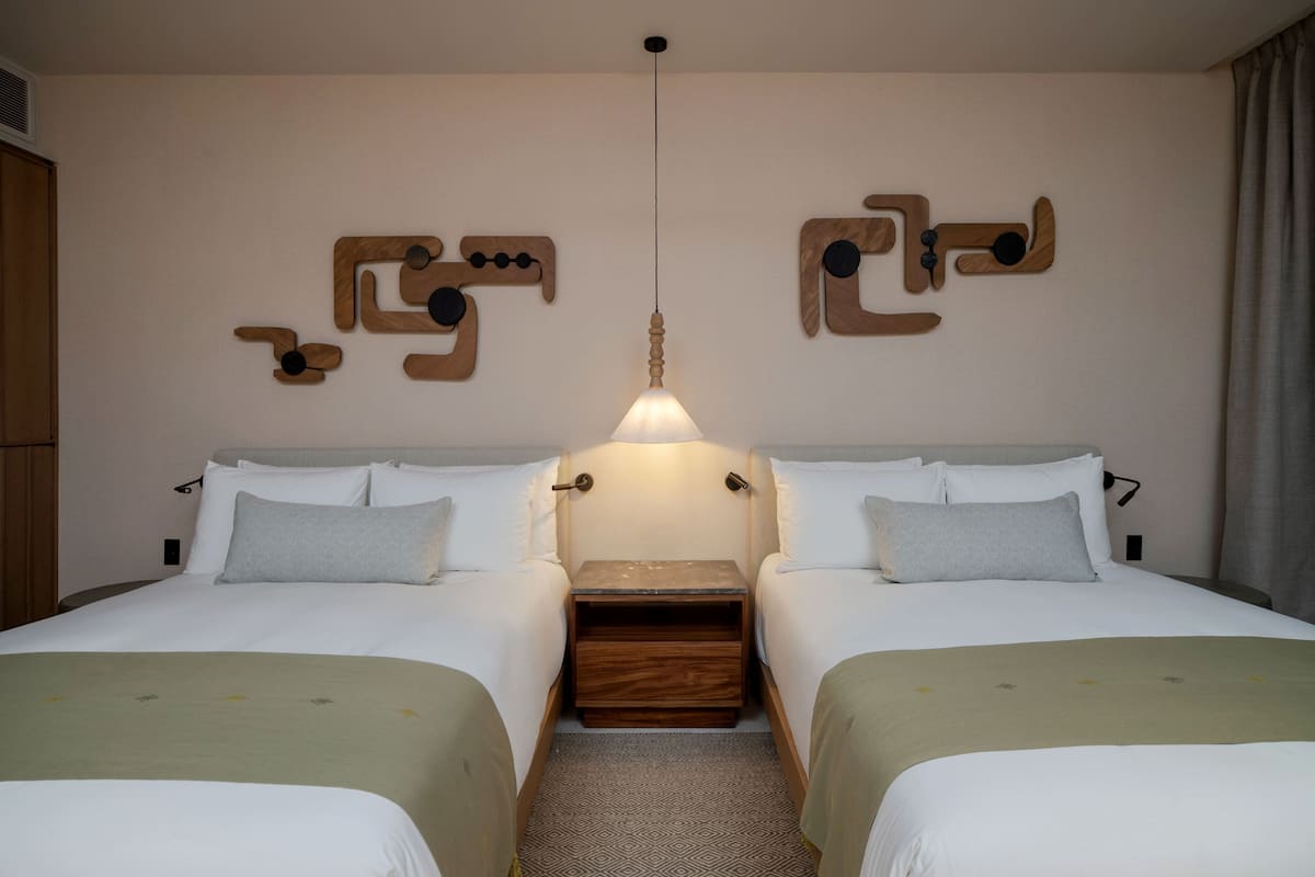 Een hotelkamer met twee bedden, een houten nachtkastje, een hanglamp en abstracte wanddecoratie.