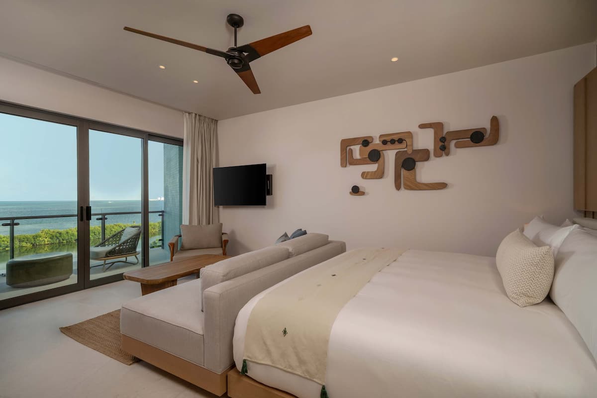 Een moderne slaapkamer met een groot bed, een bank, een televisie en een balkon met uitzicht op zee.