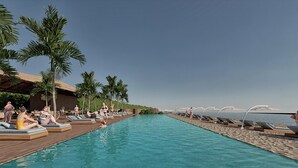 Een zwembadterras met ligbedden en palmbomen, een houten terras en uitzicht op zee.