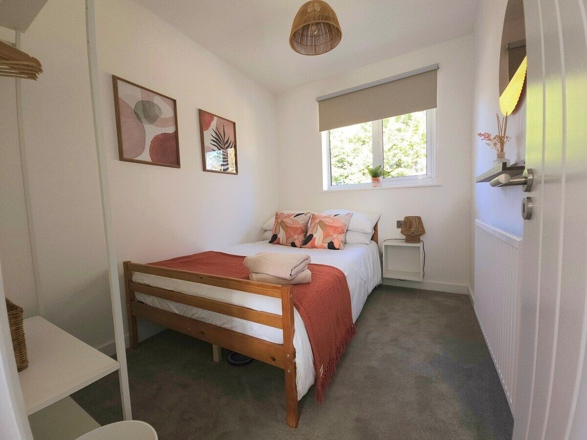 A bedroom with a wooden bed, a bedside table, a window with a view, and a wall-mounted shelf with a lamp.