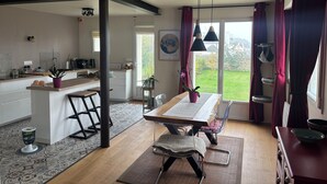 Una cocina moderna con una isla central, un comedor con mesa y sillas de madera, y vistas a un jardín a través de amplios ventanales.