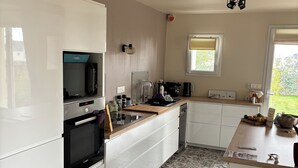 Una cocina moderna con armarios blancos, horno integrado, cafetera y ventana con vista a un jardín.