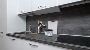 Una cocina con gabinetes blancos, encimera negra, utensilios de acero inoxidable y tabla de cortar.