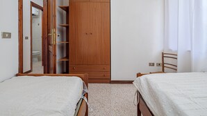 Un dormitorio con dos camas individuales, un armario de madera, un espejo y una puerta que da a un baño.
