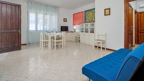 Una habitación con una mesa de comedor, sillas, un sofá, un televisor y un armario.