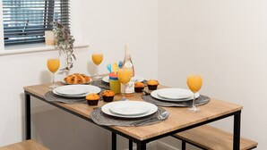 A breakfast table set with plates, glasses, muffins, and a bottle. - Central Leicester Gem | Sleeps 5 | FREE PARKING (Leicester)