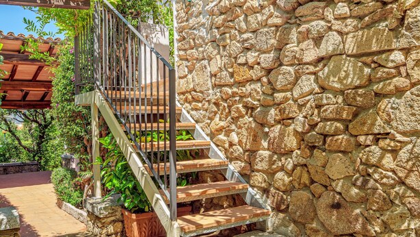 Un muro de piedra, escalones de madera y una barandilla de metal.