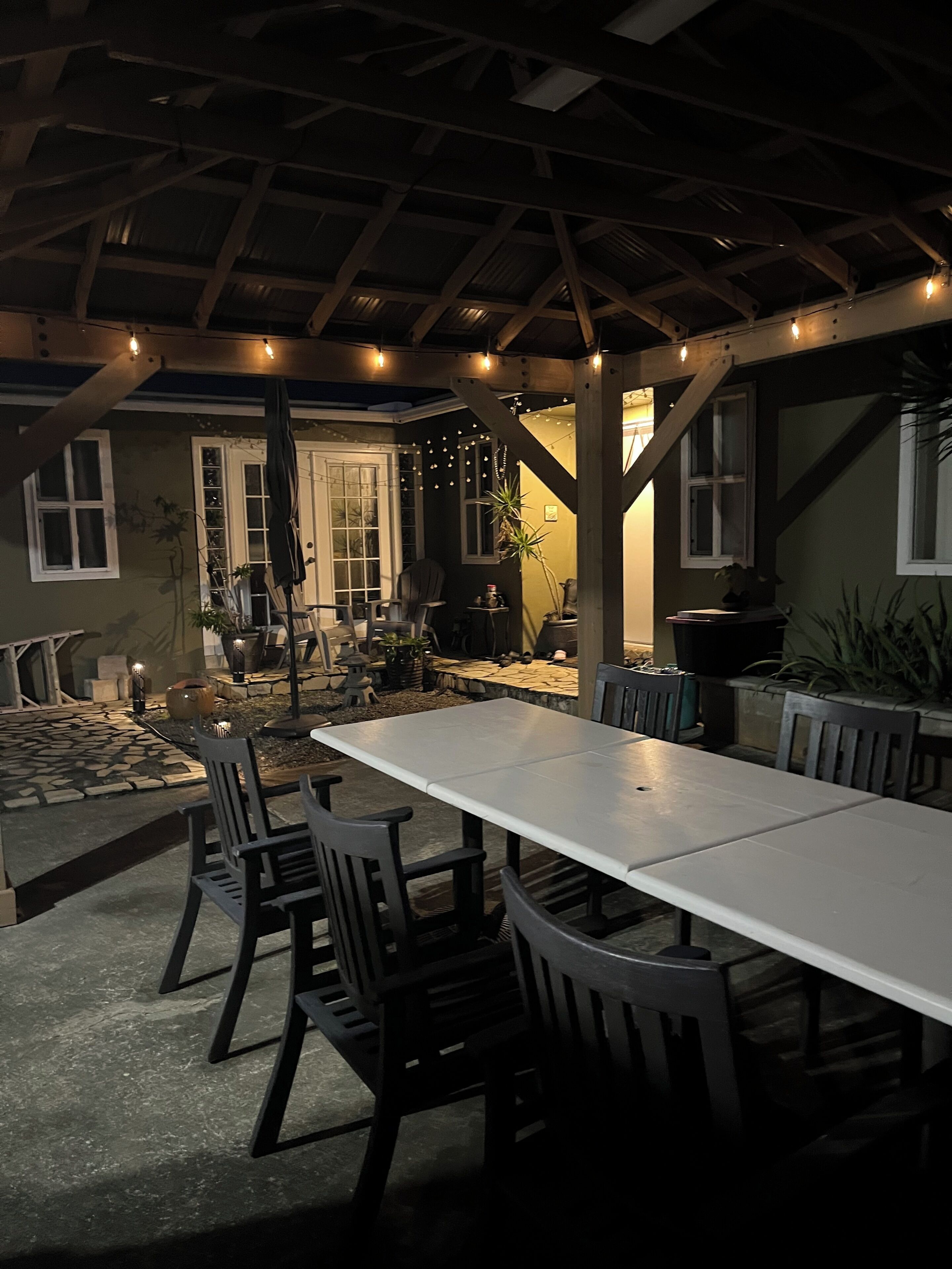 An outdoor patio with a long dining table, chairs, and string lights.