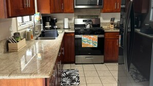Una cocina con gabinetes de madera, un microondas de acero inoxidable, un refrigerador negro y piso de baldosas.