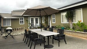 Eine Terrasse im Freien mit Tisch, Stühlen, einem großen Sonnenschirm und Kübelpflanzen.