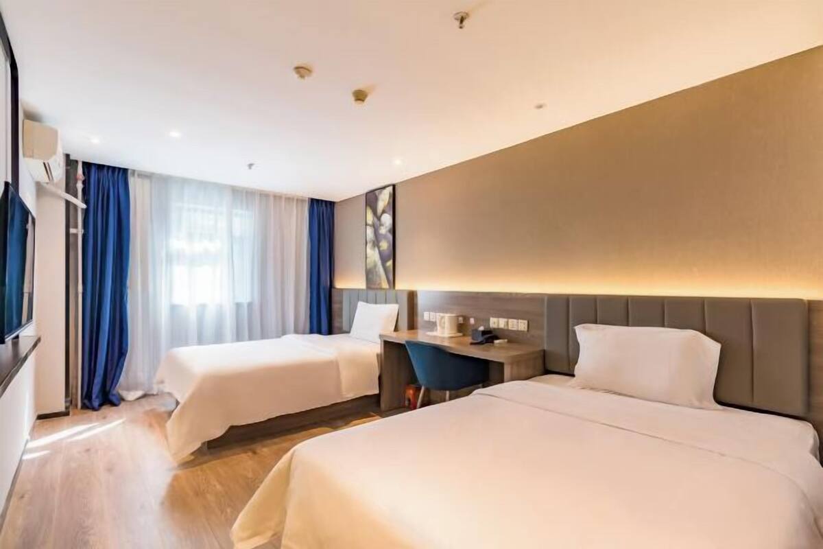A hotel room with two beds, a desk, and a large window with curtains.
