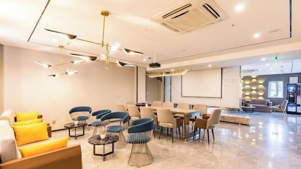 A modern hotel lobby with a seating area, a conference table, and a large screen.