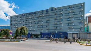 A modern hotel building with a flat facade, multiple air conditioning units, and a clear blue sky in the background.
