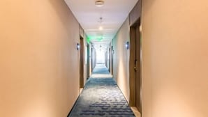 A long, narrow hotel corridor with a patterned carpet, doors on both sides, and overhead lighting.