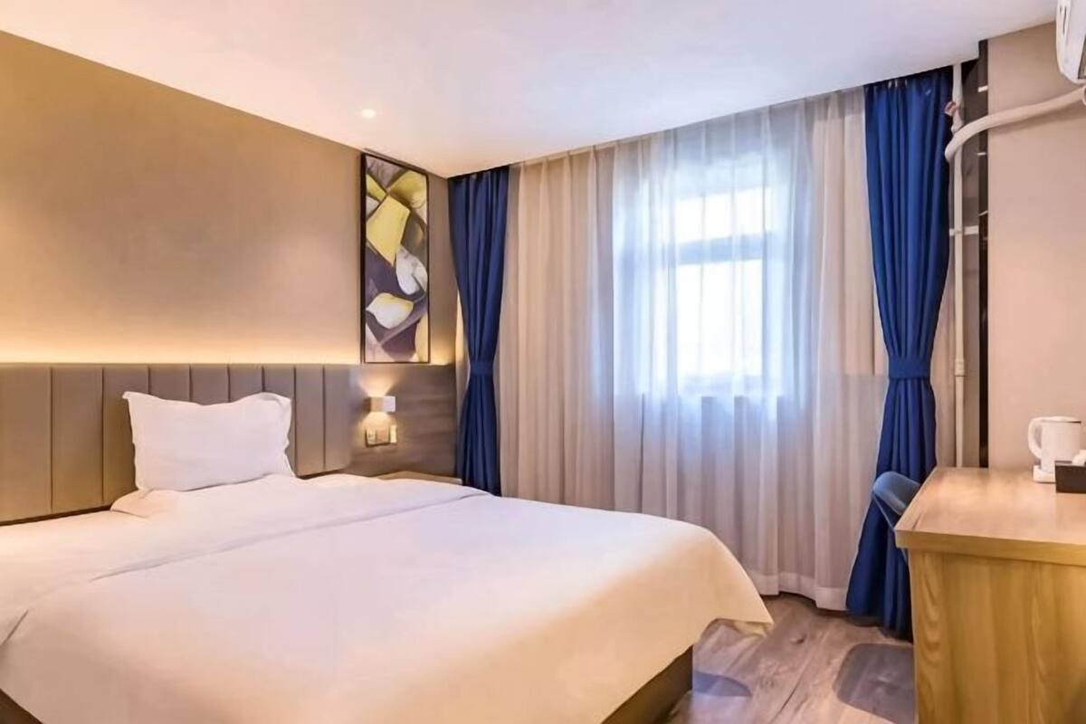 A hotel room with a bed, bedside table, lamp, and curtains.