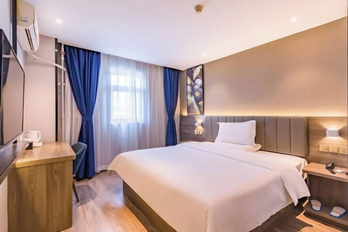A modern hotel room with a large bed, a desk, and a wall-mounted air conditioning unit.