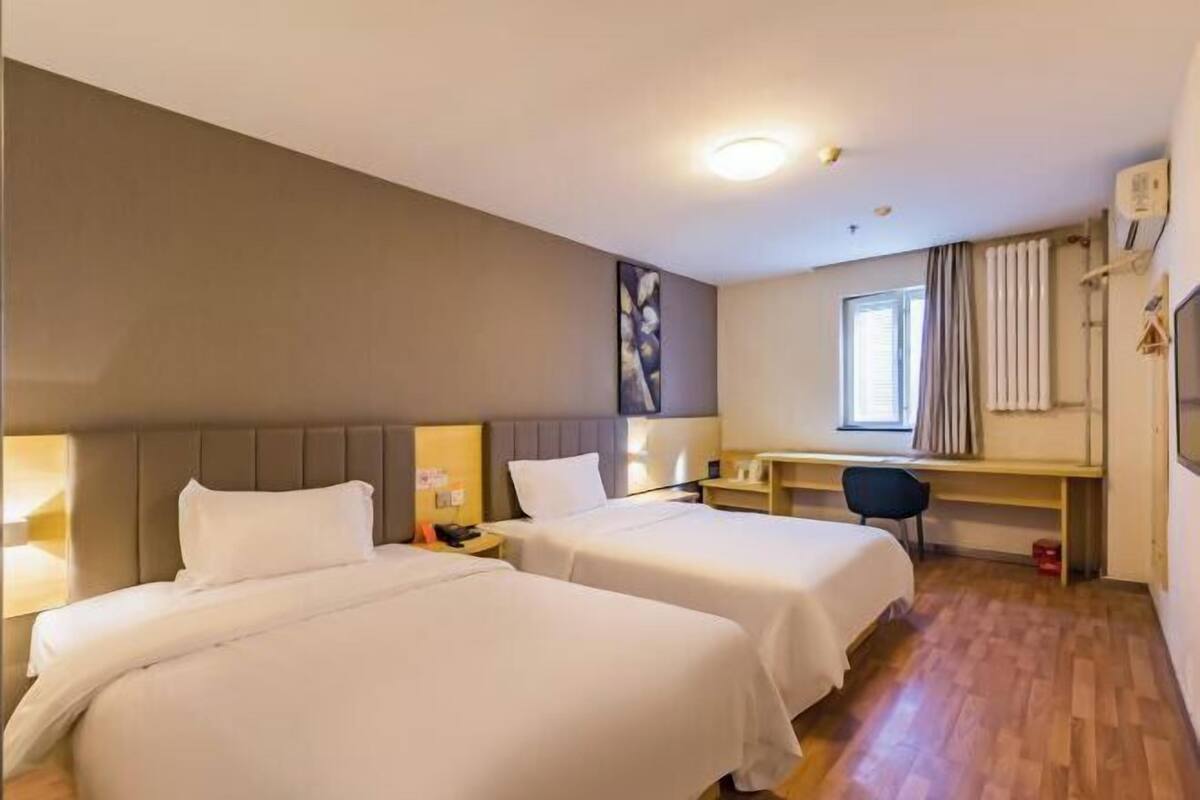 A hotel room with two beds, a desk, a chair, and a window with curtains.