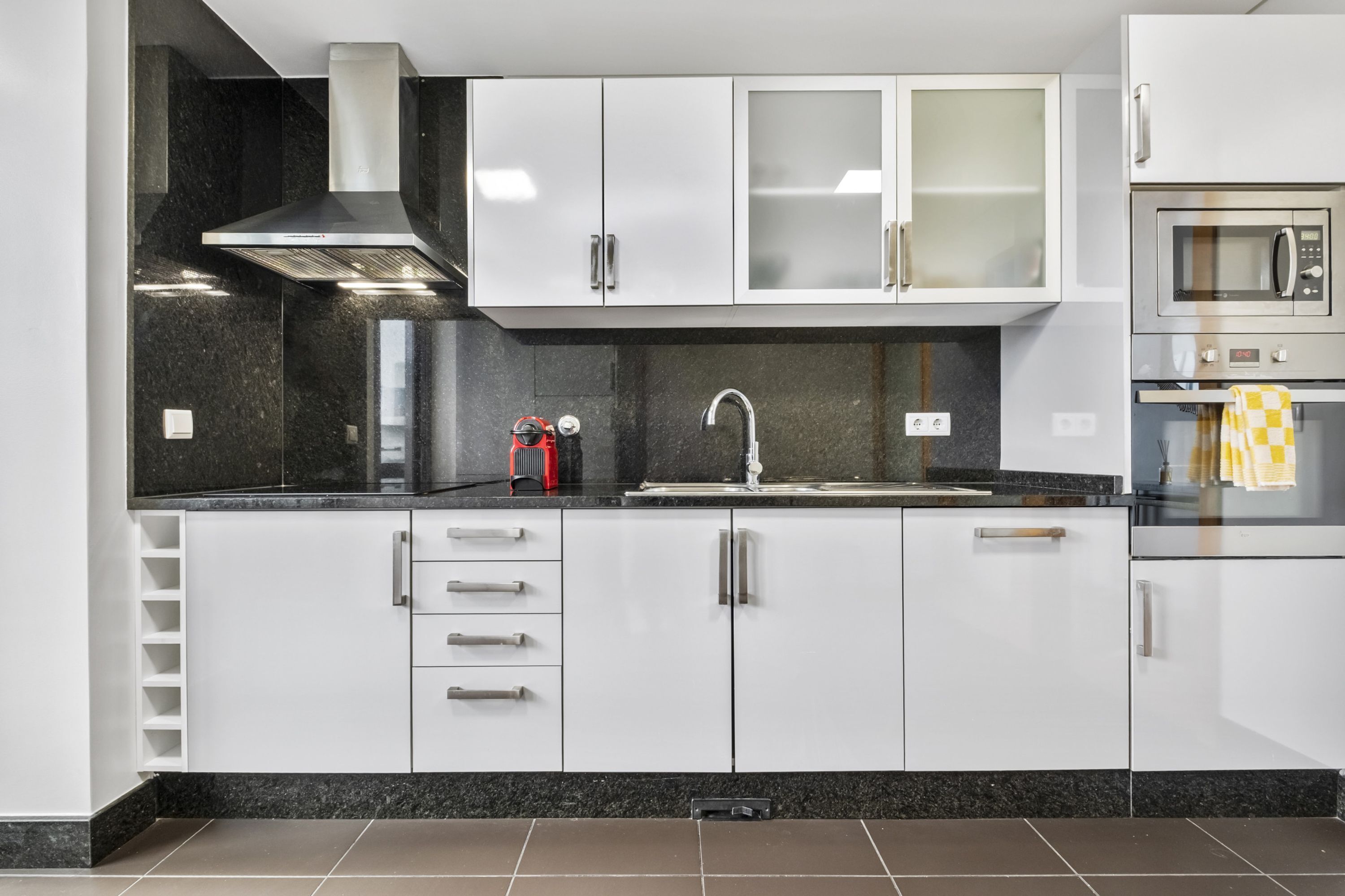 A modern kitchen with white cabinets, a stainless steel range hood, a microwave, and a sink.