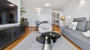 A modern living room with a grey sofa, a black and gold cabinet, a round coffee table, and a grey armchair.