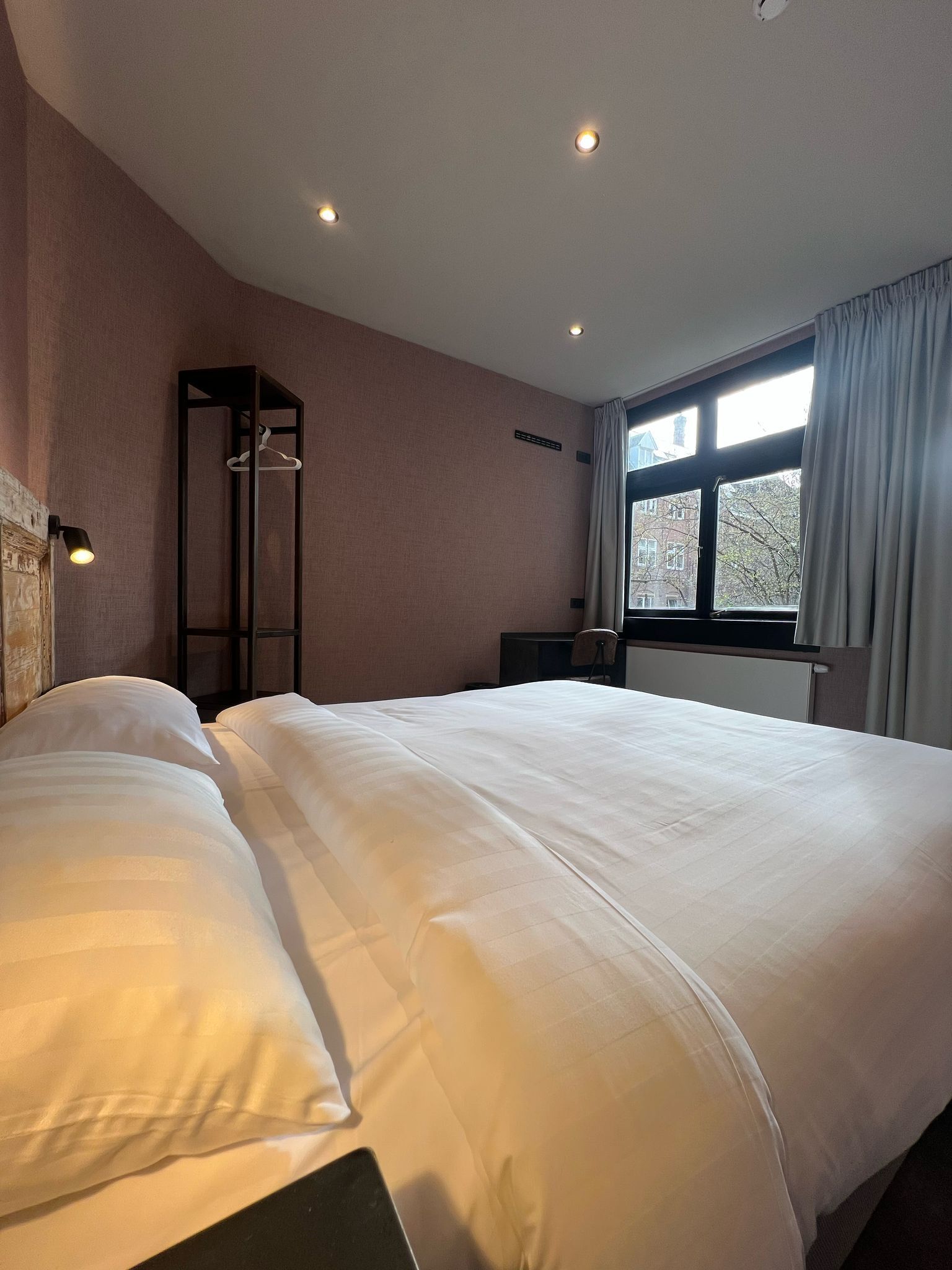 Una habitación de hotel con una cama grande, un armario, un escritorio y una ventana con cortinas.