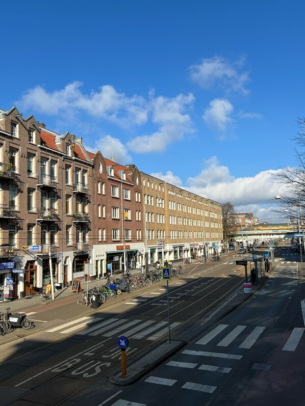 Vista de la calle con una línea de tranvía, edificios con comercios y una parada de tranvía.