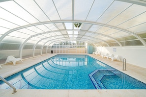 An indoor swimming pool with a glass ceiling, clear blue water, and white lounge chairs. - Apartment 'Cal Albir Atico' with Shared Pool, Wi-Fi and Air Conditioning (albir)