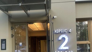 Rakennuksen sisäänkäynti, jossa on lasiovi, kyltti, jossa lukee ”KOPPYC 4 2 121–240”, ja valvontakamera.