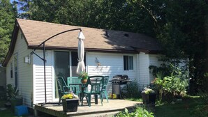 A small house with a porch, outdoor seating, a grill, and potted plants. - Cottage Retreat 75 Steps from the shores of spectacular Lake Huron, Sauble Beach (Sauble Beach)